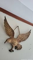 Front view of vintage brass eagle wall hanging mounted on wall with wings spread, showing detailed feathers and form.
