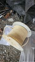 Spool of white wire placed on outdoor ground showing the wire wound neatly around the wooden spool.