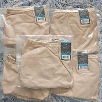 Six individually packaged pairs of light rose beige Vanity Fair briefs size 2XL laid out on a bed.