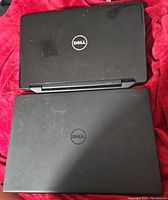 Two closed Dell laptops showing top lid with Dell logos, one larger Inspiron 15 3000 and one smaller Latitude M5040.