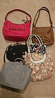 Overview photo showing five assorted women's handbags in various colors and styles placed on a beige carpet.