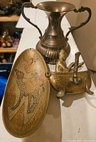 Photo showing all three brass collectible items together: trophy vase, oval tray with camel design, and bath tub figurine.