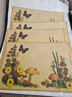 Four vintage Mid-Century Modern placemats featuring mushrooms, flowers, butterflies on beige background.