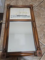 Full view of wooden framed mirror with clipper ship print mounted above the reflective glass.