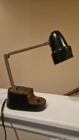 Side view of the vintage desk light showing the adjustable arm, black metal shade, and wood grain base with attached power cord.