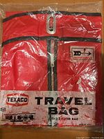 Front view of sealed red Texaco travel bag with black zipper, showing brand label and travel bag designation.