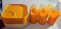 Stack of seven yellow square plastic snack plates with cup holders and three yellow plastic mugs