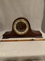 Front view of the 1930s wooden mantel clock showing its curved top, carved base, and ruler for scale.