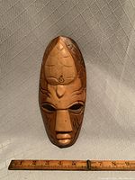 Front view of the vintage wooden wall mask lying vertically with a ruler showing length approximately 9.5 inches.
