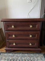 Front view of the wooden nightstand showing three drawers with brass knobs and decorative base molding.