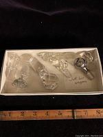 7 bottle stoppers arranged in a white box with ruler for scale, showing various shapes and sizes including one with silver overlay