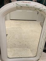 Full view of the antique mirror showing white wooden frame with hand painted green vines and red flowers and some paint chips.