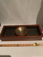 Top view of wooden dresser valet tray showing rectangular shape with dark glass and round brass bowl with emblem inlay. Ruler included for size reference approximately 14.5 inches long.