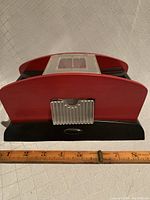 Top view of the card shuffler showing reddish wooden frame with metallic slot and black base; ruler placed for scale showing approximately 9 inches in length.
