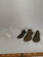 Photo showing the three antique cobbler cast iron shoe anvils in dark metal with visible use marks alongside the clear lead crystal duck figurine. A ruler is placed near the items for size reference.