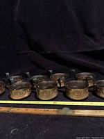 Overview of nine copper cups arranged in a row showing uniform size and details including a measuring tape indicating approximately 3 inches width.