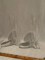 Two crystal Pilsner glasses displayed side by side on a clear background with ruler showing size approximately 9 inches tall and 6 inches wide. Unique curved boot shaped bases with swirl design clearly visible.