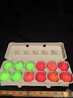 Top view of one egg carton with 18 bright neon green, pink, orange, and red Volvik golf balls.