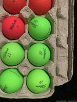Top right half of golf ball carton showing six fluorescent green golf balls with Titleist and Volvik branding and numbers.