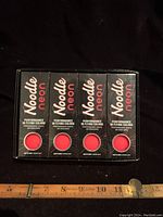 Four unopened boxes of Noodle Neon golf balls showing the front panel with brand name, color, and performance flying colors text.