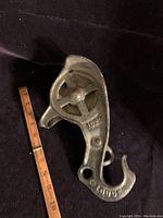 Full view of a Louden cast iron barn pulley hook next to a ruler showing about 10 inches in length