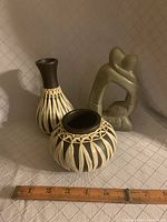 Two black Gmunder Keramik pottery pieces wrapped with raffia placed next to a stone sculpture with measuring scale in front for size reference.