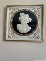 Frontal close view of the white cameo wall art in a gold and white decorated metal frame showing intricate floral patterns and beaded border.