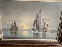 Front view of oil painting 'Boats' with several sailboats on calm water under cloudy sky, signed by artist.