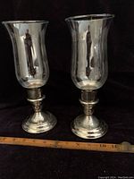 Two vintage silver plated hurricane candle holders with glass chimneys displayed side by side with measuring stick indicating height about 10 inches.