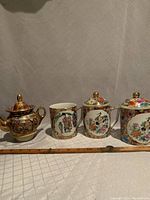 Photo shows the full lot with a small vintage Satsuma teapot and three Chinese ceramic mugs on a fabric surface with a ruler for scale.