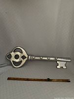 Full view of silver metal skeleton key wall rack with ruler to show size, measuring approximately 23.5 inches