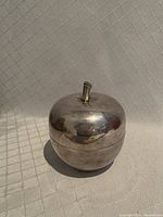 Nickel silver apple-shaped container closed showing stem detail on top and smooth reflective surface.