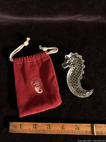 Photo showing the Waterford crystal seahorse figurine next to the red velvet drawstring pouch and ruler for scale.