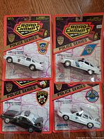 Front view of four new old stock Road Champs U.S. State Police Series diecast cars in original packaging, showing opening doors and trunks, with varying state police decals.