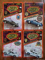 Front view of four unopened Road Champs U.S. State Police Series diecast model cars in original packaging. Each card displays the Road Champs Police Series branding, state police badges, and shows the models with opening doors and trunks.