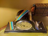 Front view of black wooden cathedral mantel chime clock featuring round clock face with Arabic numerals and painted rainbow prism and cosmic stars pattern inspired by Pink Floyd Dark Side of the Moon album art.
