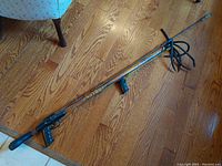 Full view of vintage Bazooka underwater spear gun showing wooden barrel and attached spear with rubber bands on hardwood floor.