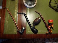 Four vintage folk art pipes arranged on a table showing variety in styles and materials including wood and stone with detailed carvings and paint.