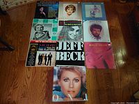 Overview photo showing all 11 vintage 33 RPM vinyl albums laid out on floor with visible titles and artist names including Jeff Beck, Anne Murray, Olivia Newton-John, The Platters, Roger Miller and others.