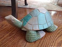 Side angle view of the handcrafted wooden sea turtle showing pastel shell colors and textured legs on wooden floor.