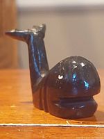 Front angled view of vintage dark stone sperm whale carving showing the whale's head, mouth details, and part of the tail.