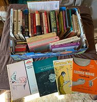 Top-down view of a box filled with assorted books including vintage repair manuals and novels