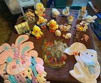 Overview of assorted Easter decorations on brown surface including plush chicks, ceramic figurines, bunny wall hangings, and other small decorations