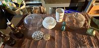 Photo showing textured white milk glass bowl, two amber Grolsch beer bottles with porcelain caps, clear glass domed cake stands, sage green pedestal dish or planter, Avon blue textured glass bottle, white mug, and small decorative glass items.