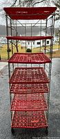 Front view of bread rack showing seven red plastic shelves and metal frame, with some shelves cracked