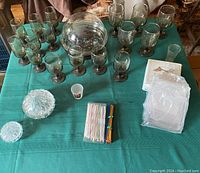 View of the full lot from above showing crystal Hershey Kiss candy dishes, numerous smoky glass stemmed glasses, colorful plastic stir sticks, acrylic coasters, and glass terrarium domed lid.