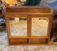Front view of solid oak medicine cabinet with two beveled glass mirrored doors, showing natural wood grain and decorative top edge.
