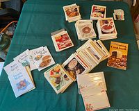 Wide view showing various stacks of recipe cards and a yellow cookbook on a green tablecloth.