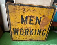Front side of the metal traffic sign showing the text 'MEN WORKING' in black on a yellow background with visible rust, scratches and wear.