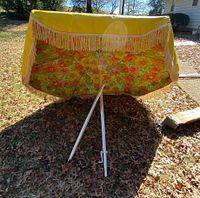 Open umbrella showing yellow exterior, floral pattern underside, white pole, and fringe trim.
